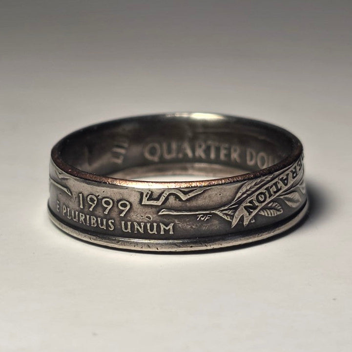 A silver-colored coin ring made from a 1999 US quarter dollar, featuring the Native American head and the inscription 'E PLURIBUS UNUM' on the front, photographed on a neutral light gray background.
