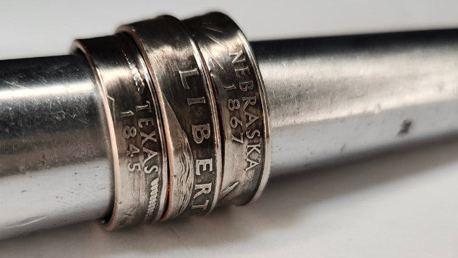A close-up of a silver-toned metal ring with engraved text, shown on a white surface with black letterboxing above and below.